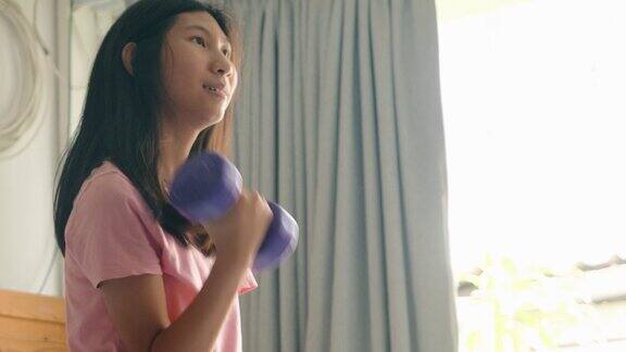 亚洲女孩在家和哑铃在窗户附近锻炼健康的生活方式理念