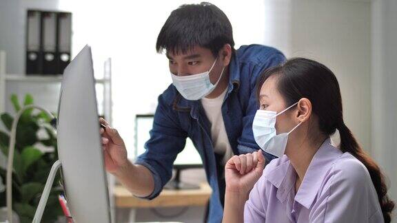 两名亚洲商务人员在电脑上开会与同事们戴着防护口罩头脑风暴关于新项目的想法新常态的办公室