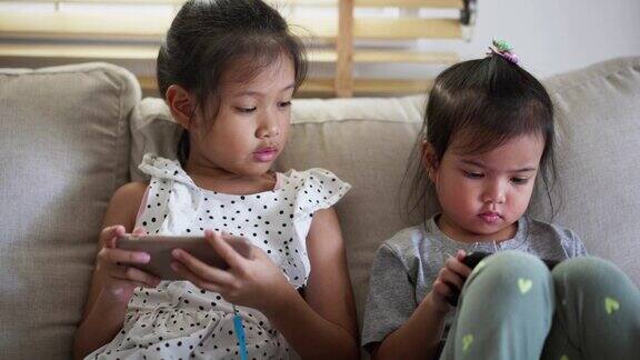 兄弟姐妹坐在沙发上一起在家里玩网络手机游戏孩子玩智能手机玩得很开心