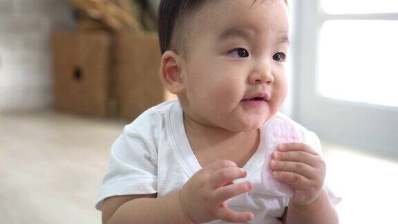 可爱的亚洲婴儿坐在舒适的房间地板上咬零食