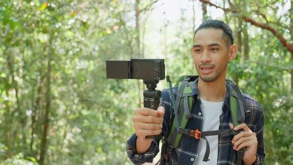 亚洲英俊男性背包客视频博主独自在森林里旅行魅力男旅行者用手机录制视频在大自然的树林里散步带着幸福的假期旅行