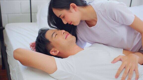 亚洲妻子躺在卧室的床上亲吻丈夫美丽的新婚夫妇穿着睡衣感觉幸福和放松在清晨一起在家里度过闲暇时间