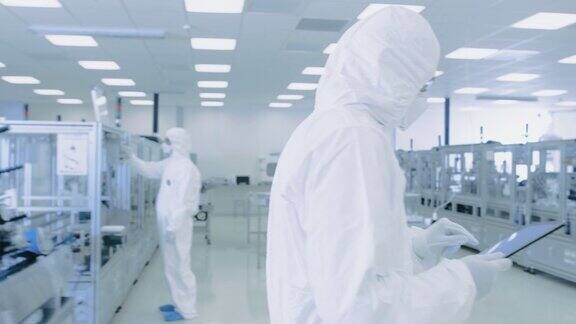 科学家使用数字平板电脑和穿着防护服走过制造实验室与现代工业机械产品制造工艺:制药半导体生物技术