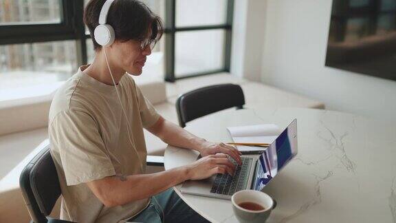 专注的亚洲男人在笔记本电脑上工作喝着咖啡