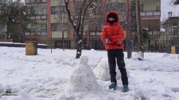 下雪天穿红外套的男孩在操场上堆了一个雪人