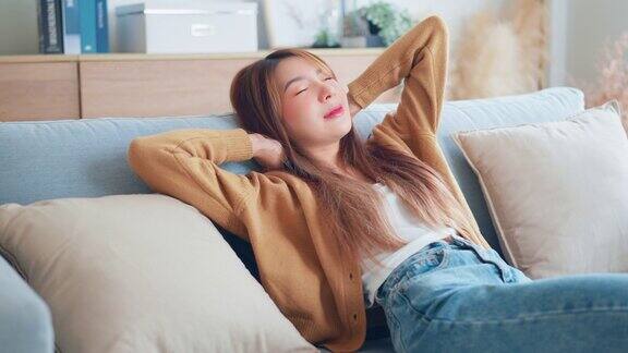 放松的年轻亚洲女子享受休息在舒适的沙发在家里冷静有吸引力的女孩放松和呼吸新鲜的空气在家里