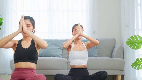 亚洲活跃的女性朋友在家里一起做瑜伽普拉提锻炼漂亮的女孩穿着运动服在家里的客厅里用垫子花空闲时间健身保健