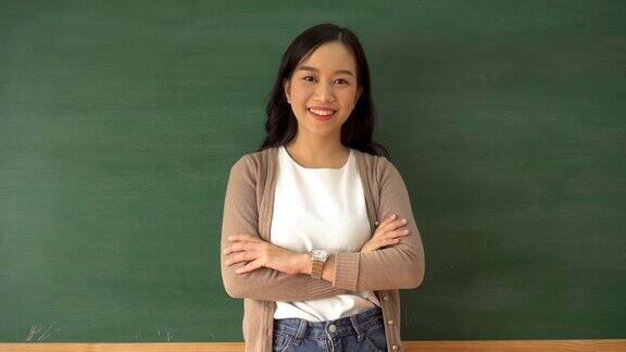 年轻的亚洲女教师在学校教室的黑板前微笑