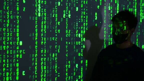 男性黑客在电脑上工作而绿色的代码字符反映在他的脸上