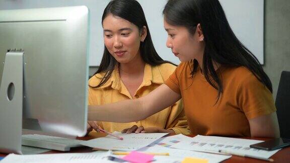 两个亚洲商务办公室的妇女讨论想法而工作与台式电脑在办公室