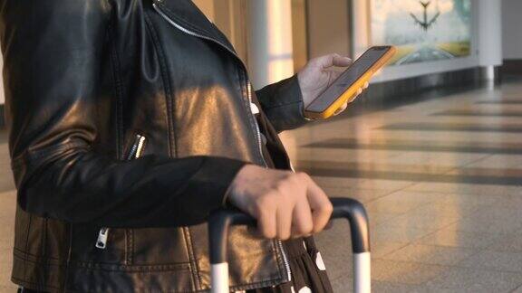 一名身穿黑色夹克的女子拎着行李箱站在机场检查她的智能手机
