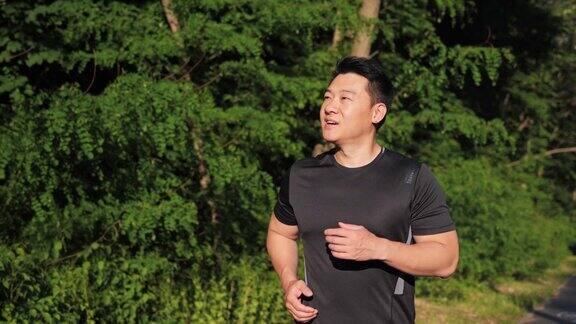 英俊的中国运动员在日落时跑步一名跑步者在公园跑步的肖像背景是夕阳下的绿树户外运动训练街头运动运动员在户外训练