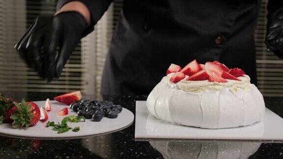 糕点师用新鲜水果和薄荷叶装饰安娜·帕夫洛娃的蛋糕