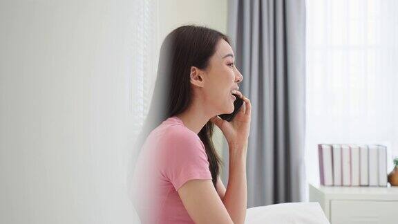 亚洲有魅力的女人早上在家的床上打电话快乐休闲美丽的女性坐在卧室里享受假期周末在家里使用智能手机与技术交流