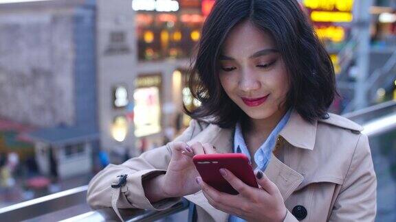 一个相当快乐的年轻亚洲女人在晚上使用手机在城市