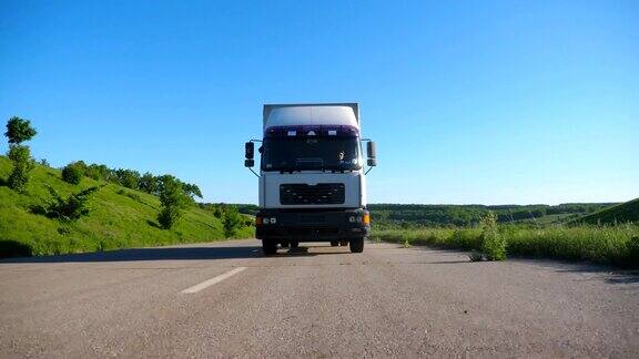 卡车正面视图与货物拖车行驶在公路上运输货物在夏季的一天白色的卡车驶过乡村背景是美丽的自然景观慢动作