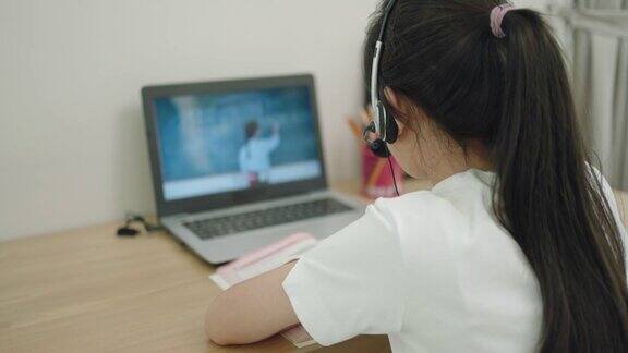 一名亚洲少女在学校因新冠肺炎疫情关闭期间在家中的客厅通过笔记本电脑与老师在线学习数学