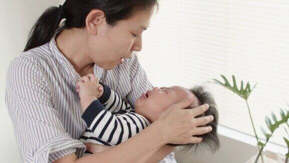 年轻的亚洲母亲抱着并安慰哭泣的新生儿