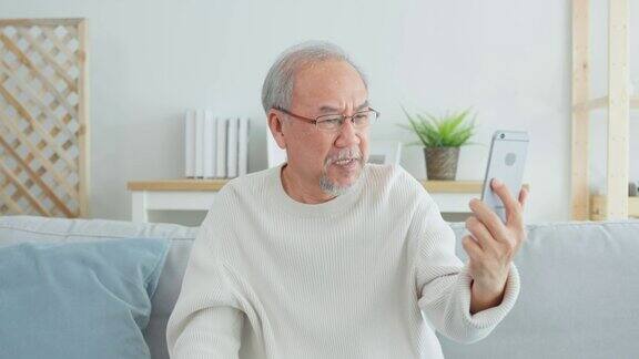 亚洲老年男子在客厅用手机进行视频通话有魅力的老年男性坐在沙发上用智能手机与家人进行视频会议感到很开心