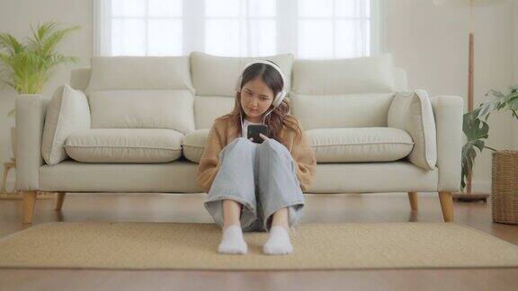 快乐的年轻亚洲女人在家里放松女性微笑着坐在沙发上手里拿着手机女孩用视频电话给朋友