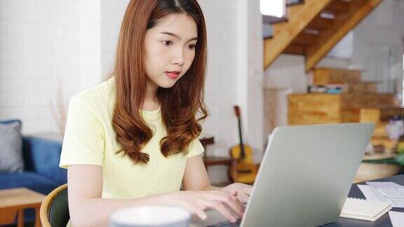 自由职业亚洲女性的肖像穿休闲装使用笔记本电脑在家里的客厅工作