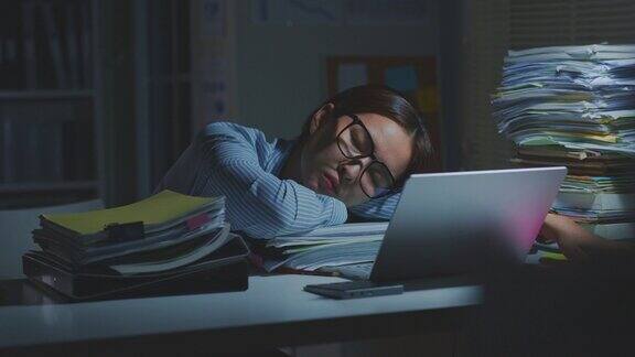 过度工作的年轻亚洲办公室员工睡觉同时在办公室的笔记本电脑加班