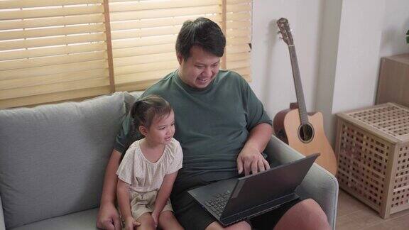欢快的家庭父亲和他的女儿一起享受在家里的客厅用笔记本电脑看视频