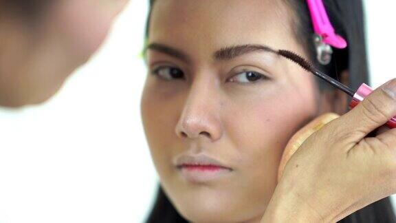 亚洲女性用特殊的眉刷在年轻女性的皮肤上涂眉粉