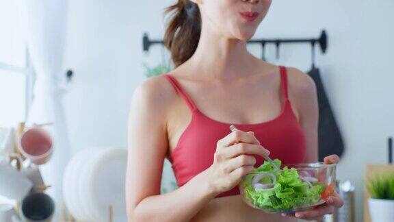特写亚洲美女端着沙拉碗吃蔬菜漂亮的运动女孩穿着运动服在家里享受运动后吃干净的蔬菜的健康饮食和健康食品