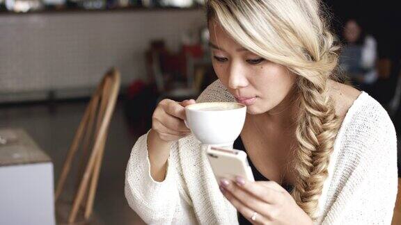一段4k视频一名美丽的年轻女子在咖啡馆边喝咖啡边查看她的社交动态