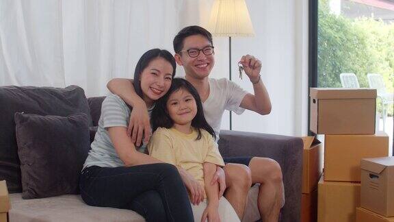 肖像亚洲年轻家庭买了新房日本学龄前的小女儿和父母手拿钥匙坐在客厅的沙发上笑着看着镜头