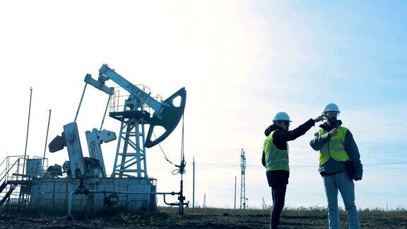 两名男子站在油田上背景是一座石油塔