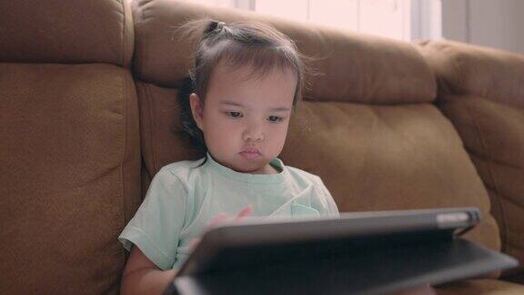 一个亚洲小女孩喜欢坐在沙发上玩平板电脑