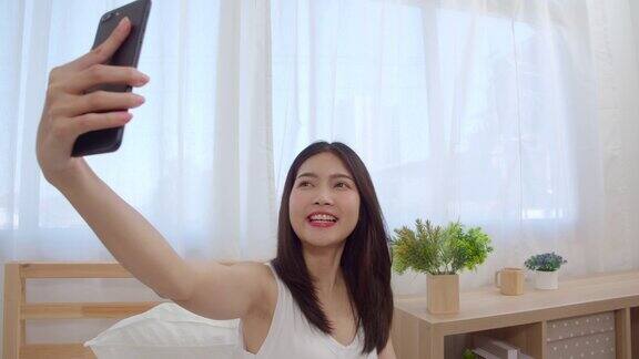 年轻的亚洲少女在家里做视频博客女性在卧室里用智能手机制作视频到社交媒体生活方式女人在家里放松上午慢动作镜头