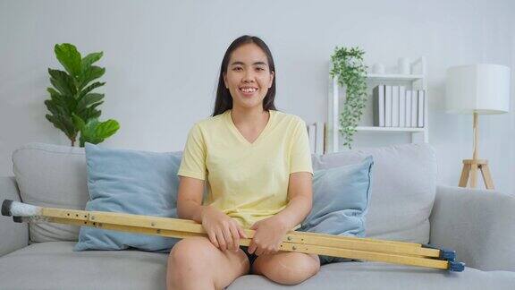 亚洲年轻截肢腿女子的肖像微笑着看着相机迷人的女性没有腿感到快乐和放松独自坐在沙发上享受周末活动的生活方式在早上在家里