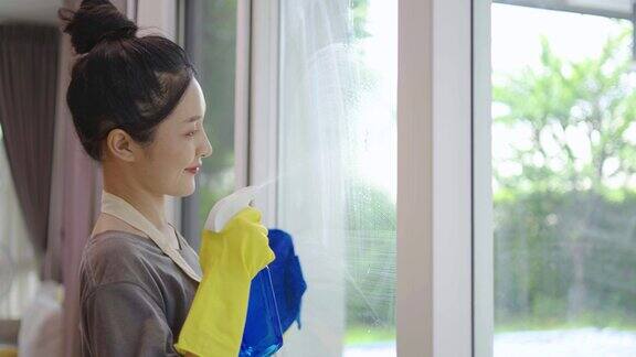 开朗积极的亚洲年轻女子戴着黄色防护橡胶手套在家里用抹布和清洁剂喷雾清洁窗户享受家务愉快地做家务