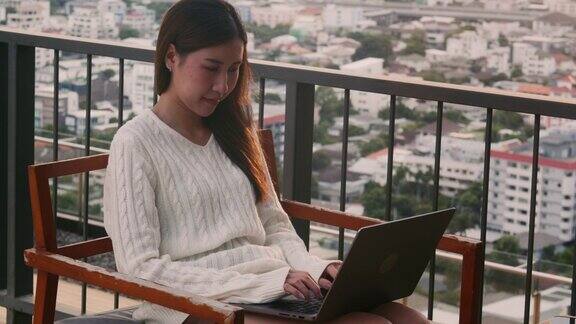 年轻的亚洲女商人穿着休闲服装在日落时分用笔记本电脑工作