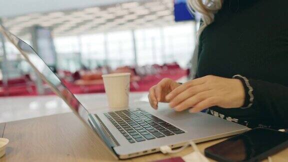 在机场候机室一位女士一边喝咖啡一边用智能手机和笔记本电脑