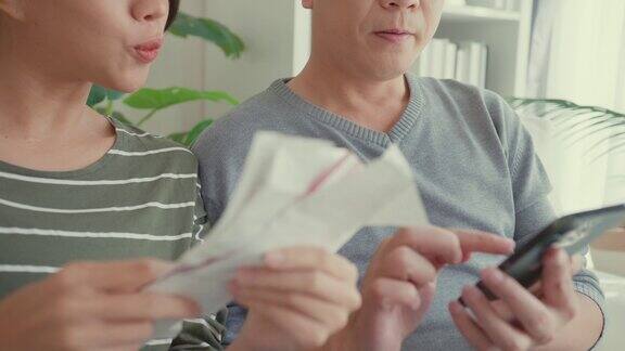 亚洲夫妇用电话计算近照水电费计算支票信用卡收据每月开支账单一起坐在家里客厅的沙发上生活方式花时间在家里