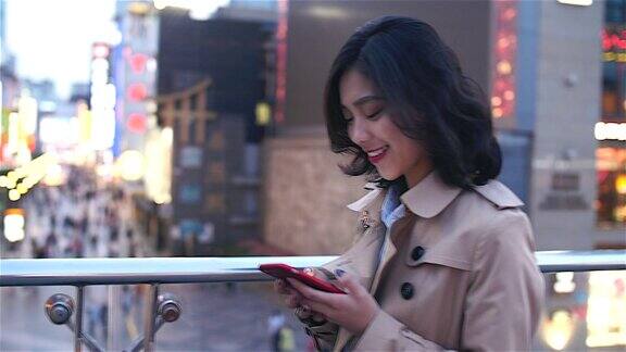 在中国成都一名非常快乐的年轻亚洲女子正在使用手机她正走在天桥上背景是繁忙的街道