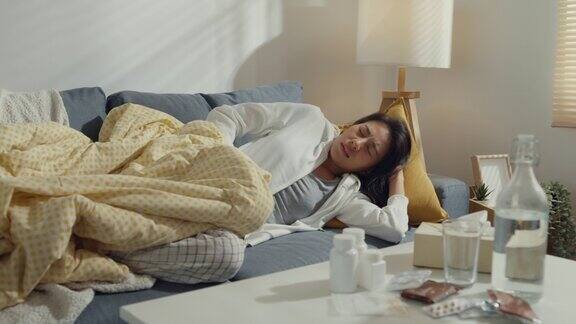 生病的年轻亚洲妇女遭受强烈的腹部疼痛躺在毯子下的沙发在家里的客厅