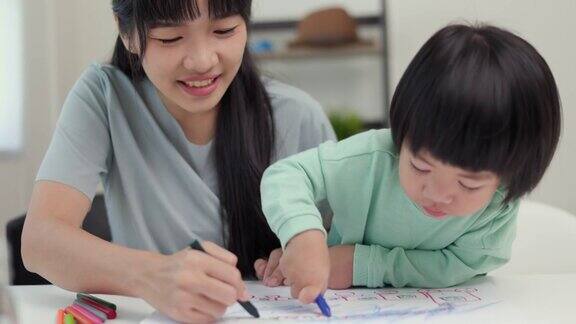 妈妈教儿子如何用蜡笔在书上画画或做作业快乐的亚洲男孩与他的母亲在客厅里用蜡笔和彩色铅笔画画家庭
