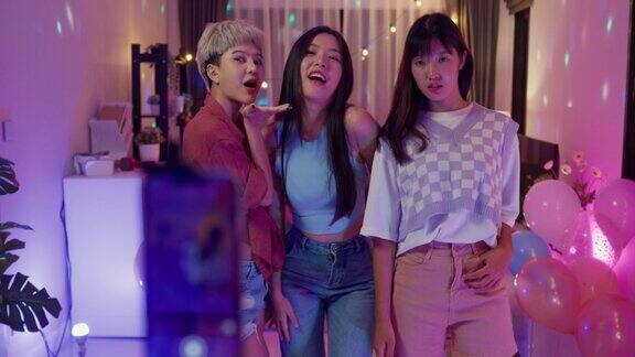 年轻的亚洲女性朋友在晚上用智能手机自拍在多彩的家庭派对上玩得很开心