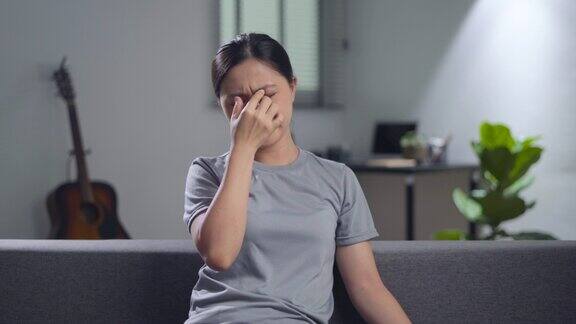 一名亚洲妇女坐在家里的沙发上眼睛疼得难受