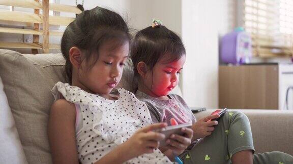 兄弟姐妹坐在沙发上一起在家里玩网络手机游戏孩子玩智能手机玩得很开心