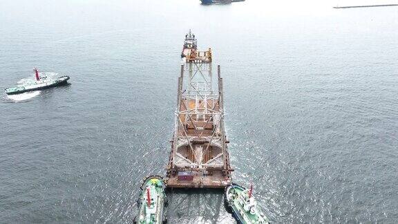 拖船拖着船上的大型建筑驳船运输平台上的招标钻井平台到海洋中央的石油钻井平台