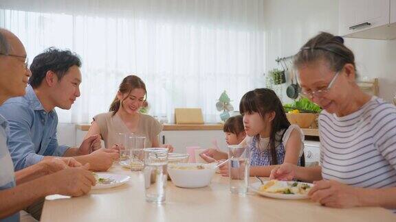 亚洲大家庭在家里的餐桌上一起吃午餐年迈的爷爷奶奶、年轻的夫妇和年幼的女儿们感到幸福在家里享受美食活动关系概念