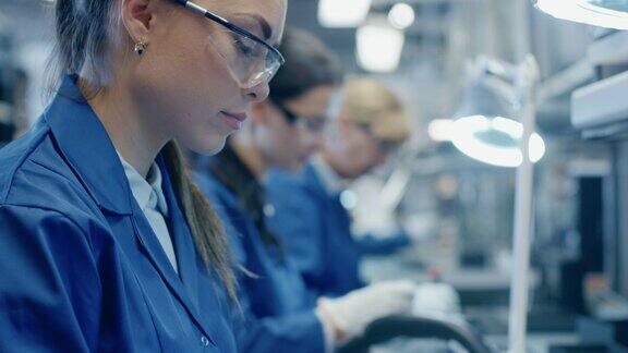 穿着蓝色工作服和防护眼镜的电子厂女工正在用镊子组装智能手机的印刷电路板拥有更多员工的高科技工厂