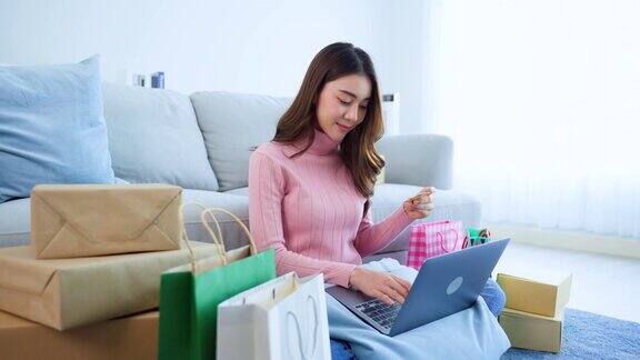 亚洲美女在家客厅享受网上购物漂亮女孩坐在地板上用笔记本电脑在网上商店购物后手持信用卡进行网银网上支付