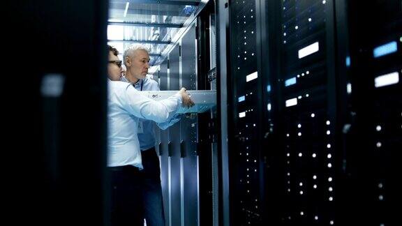 2名服务器技术人员在服务器机架中安装硬件他们在大型现代数据中心工作